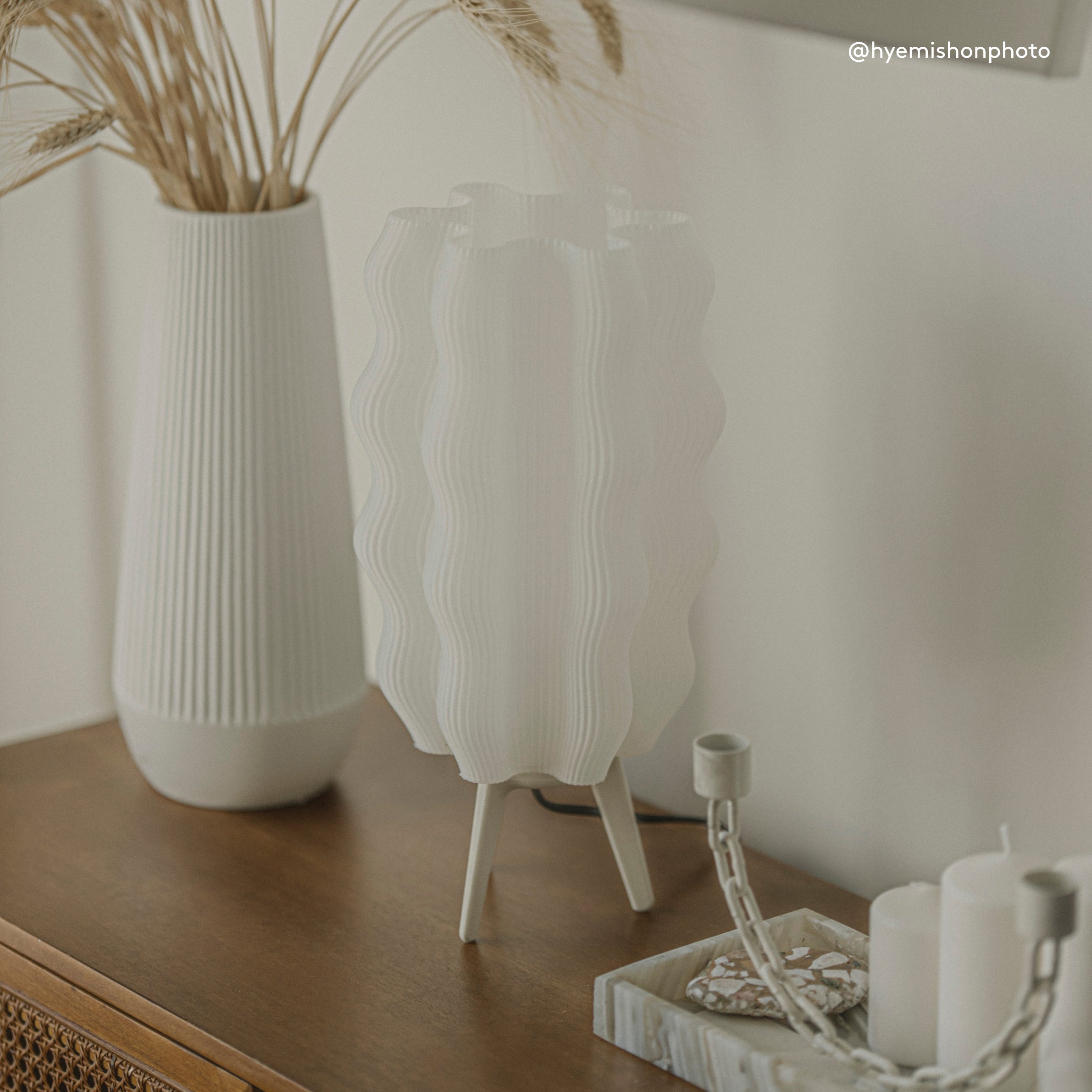 Decorative setup with white vases, candles, and dried plants on a wooden surface.
