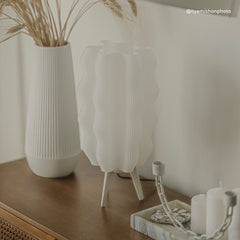 Decorative setup with white vases, candles, and dried plants on a wooden surface.