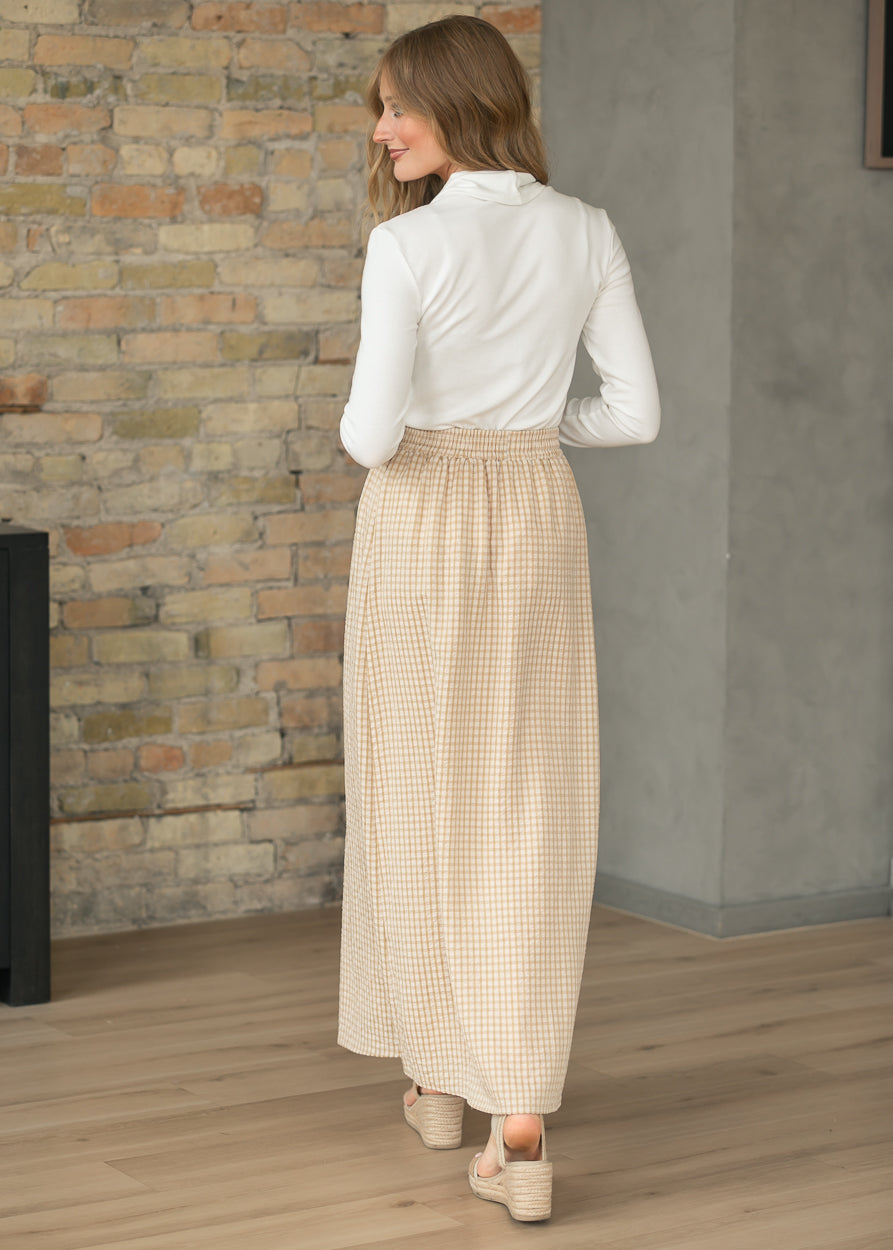 Woman wearing a white blouse and beige checkered skirt standing in a room with a stone wall.