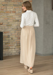 Woman wearing a white blouse and beige checkered skirt standing in a room with a stone wall.
