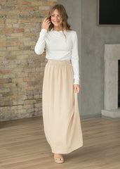 Woman wearing a white top and beige checkered skirt standing in a room with a brick wall and fireplace.