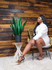 Woman sitting on a chair next to a potted plant against a wooden wall.