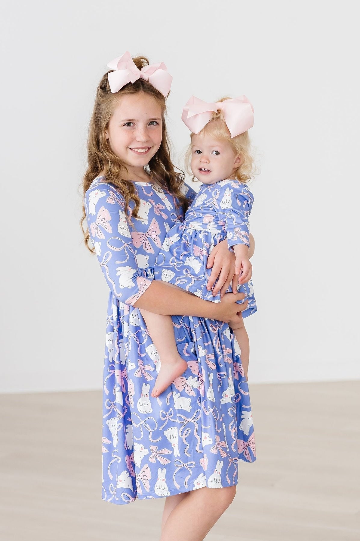 Two young girls wearing matching blue dresses with floral patterns, standing against a plain background.
