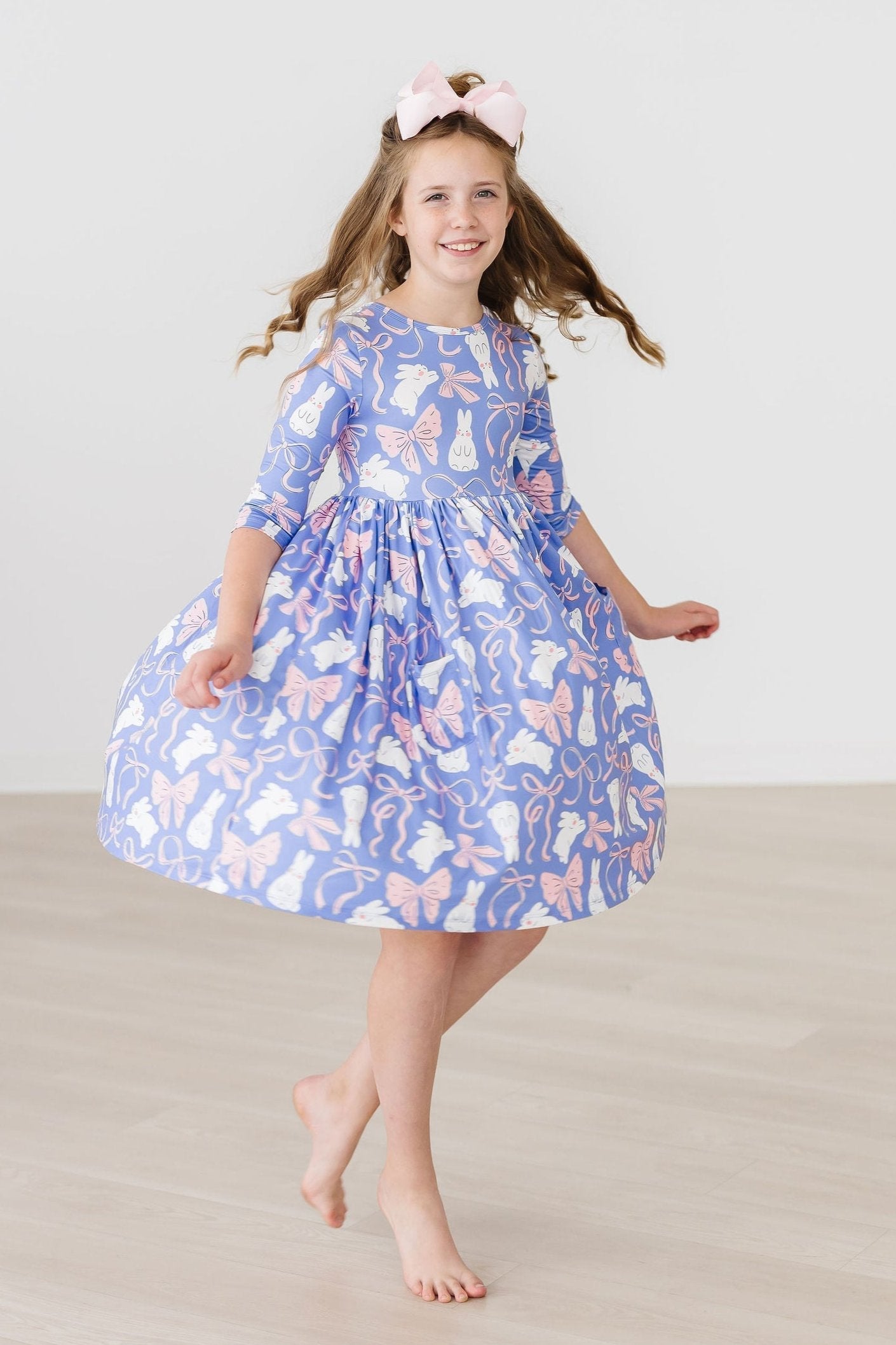 Young girl wearing a blue dress with pink floral pattern on a plain background