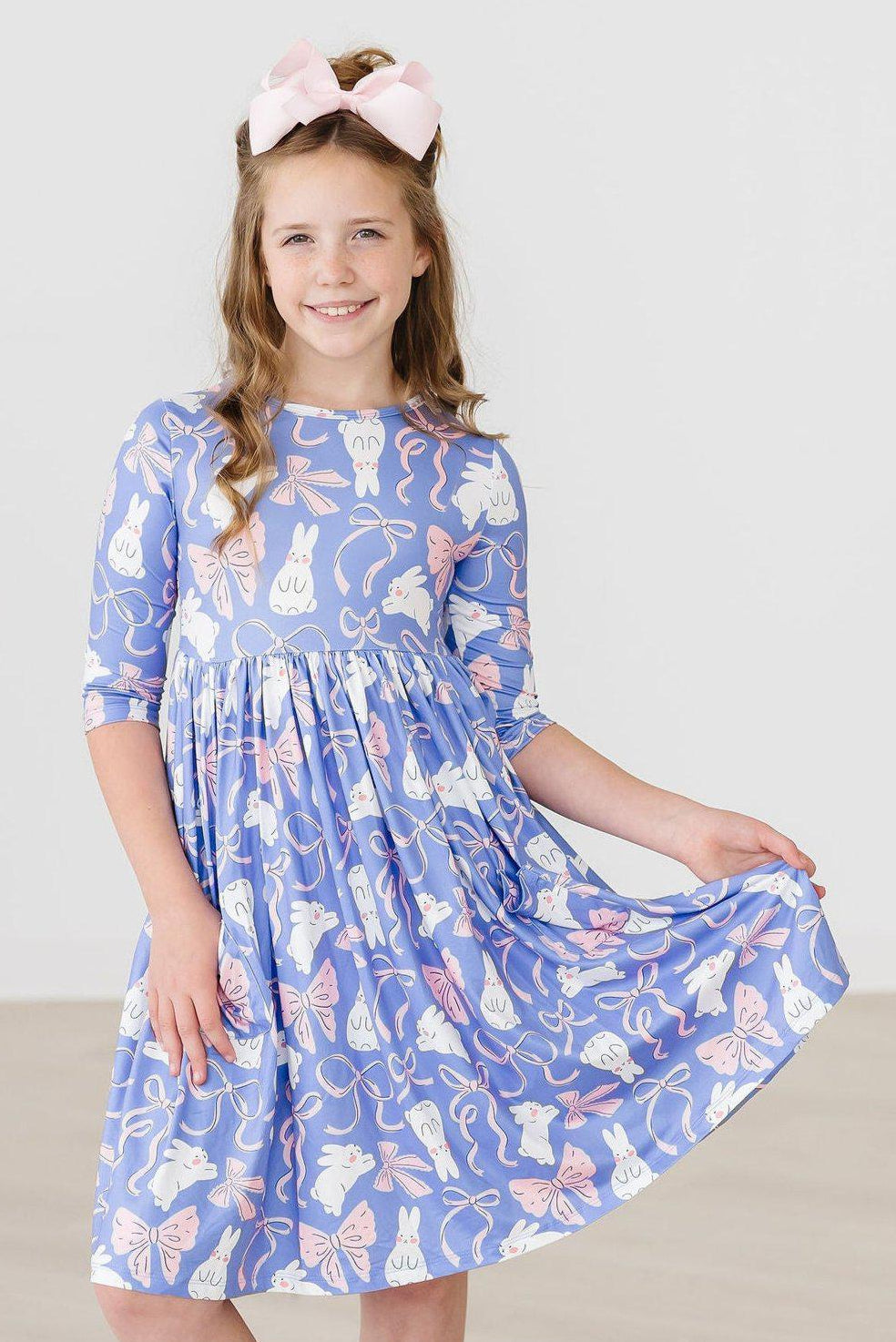 Young girl wearing a blue dress with cat and bow pattern on a white background