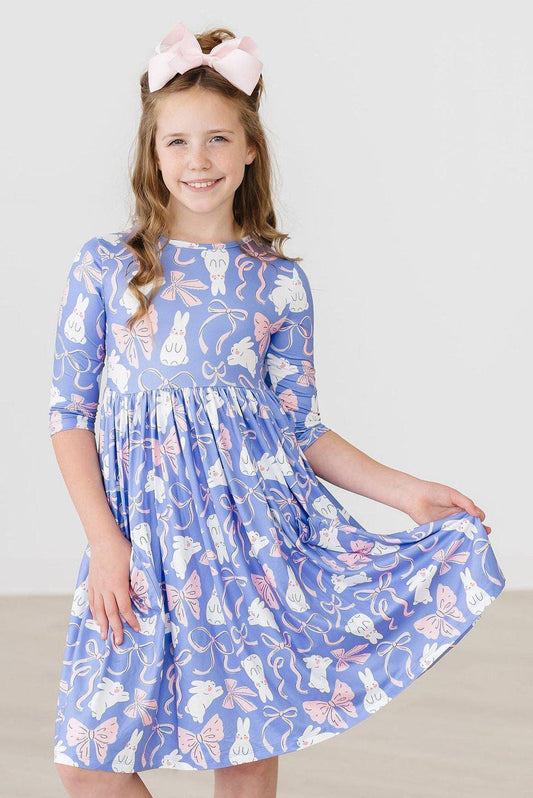 Young girl wearing a blue dress with cat and bow pattern on a white background