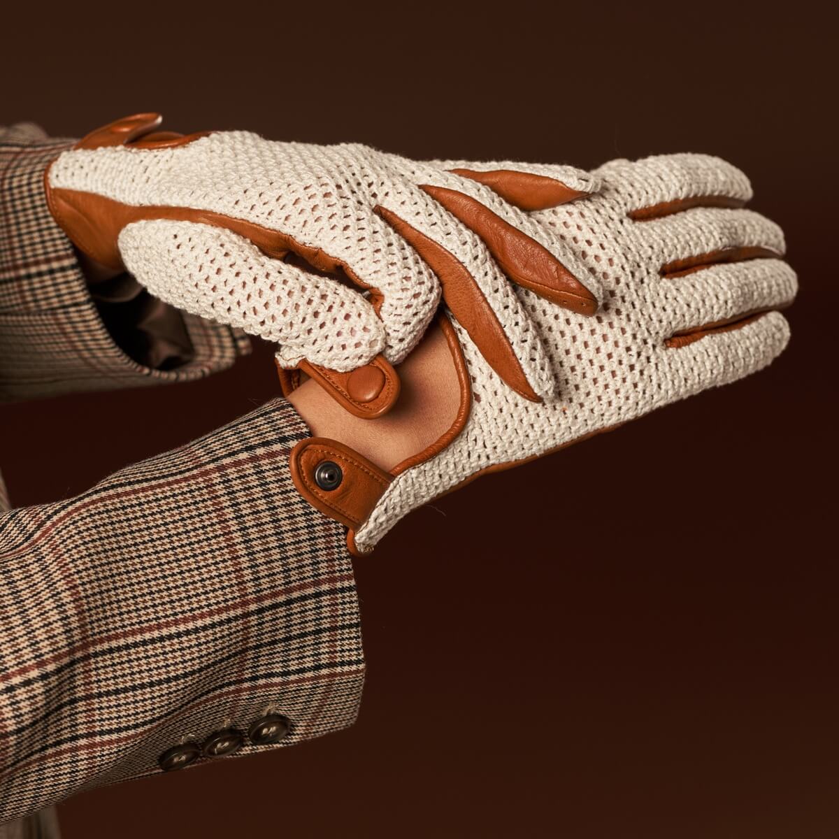Close-up of a beige and brown glove with a plaid jacket on a dark background
