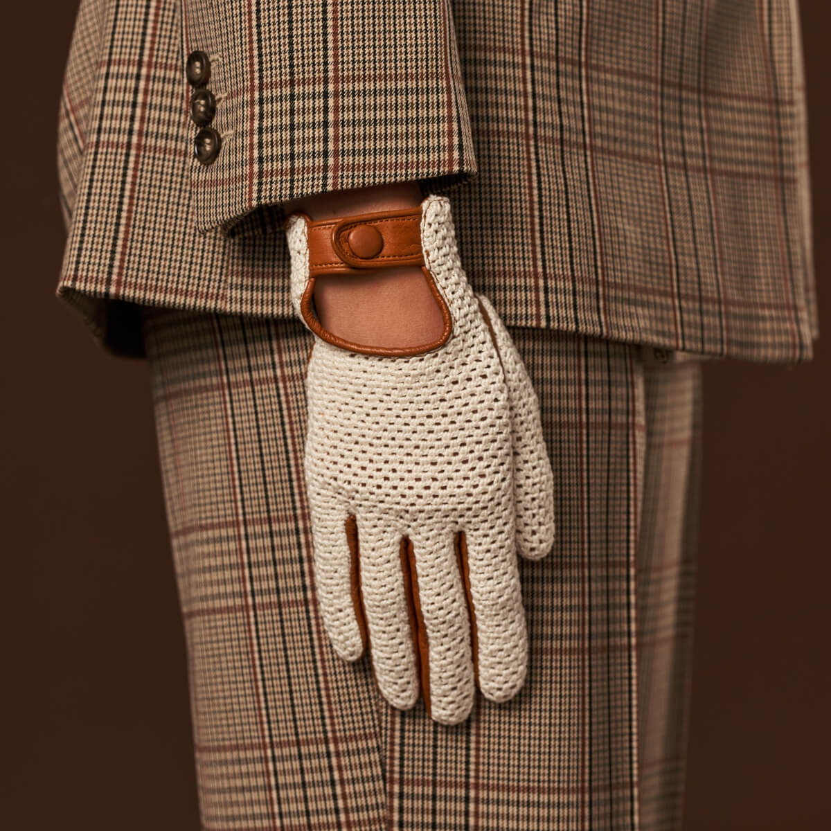 White knitted glove with brown leather patch on a plaid suit background