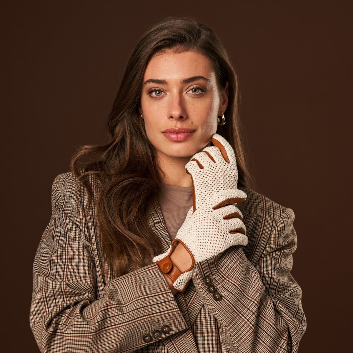 Woman wearing a plaid coat and white gloves with brown leather accents on a brown background
