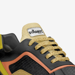 Close-up of a sneaker with gold laces and 'BY MANYC' branding on a white background