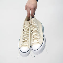 White high-top sneakers being held against a white background