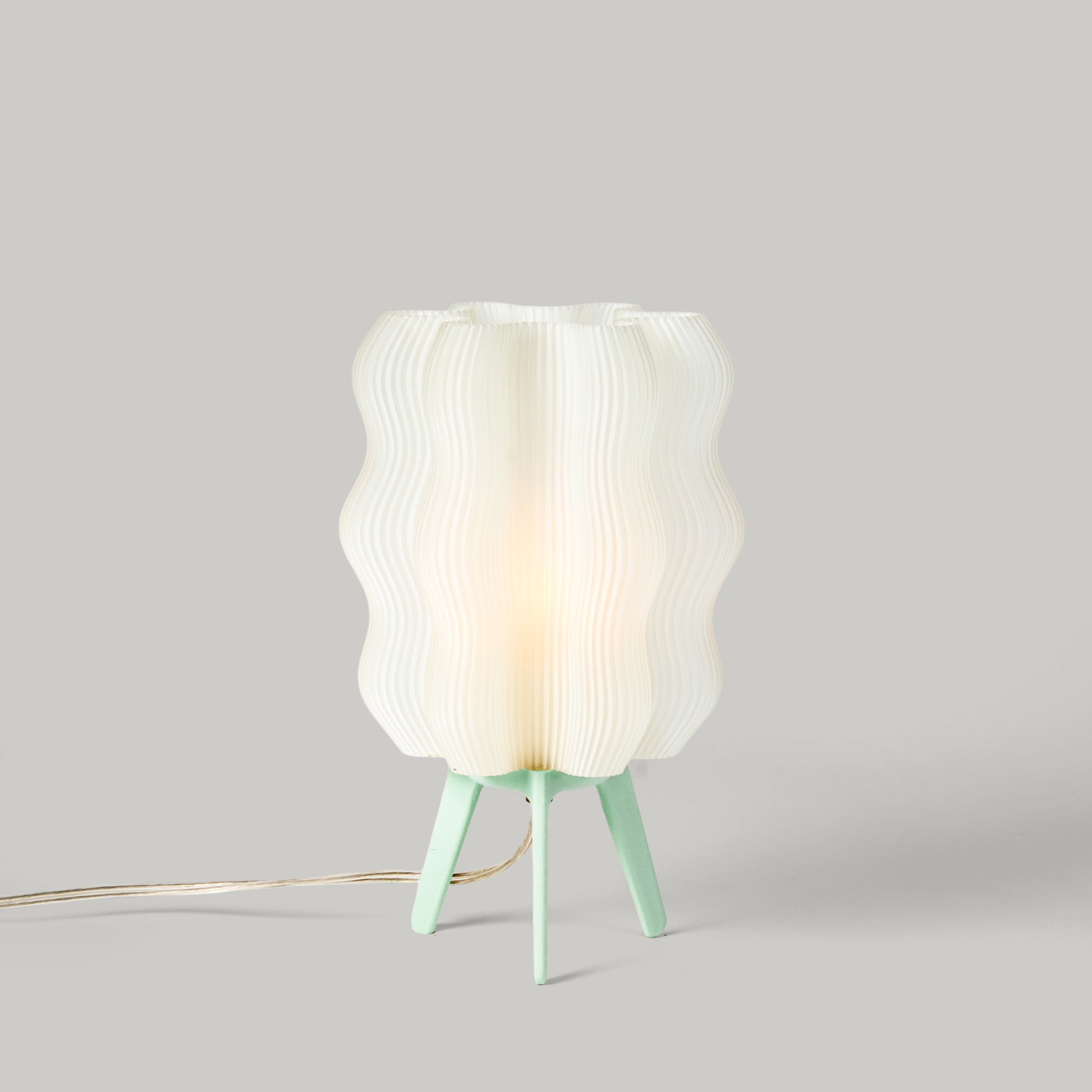 Table lamp with a textured white shade and green base on a gray background