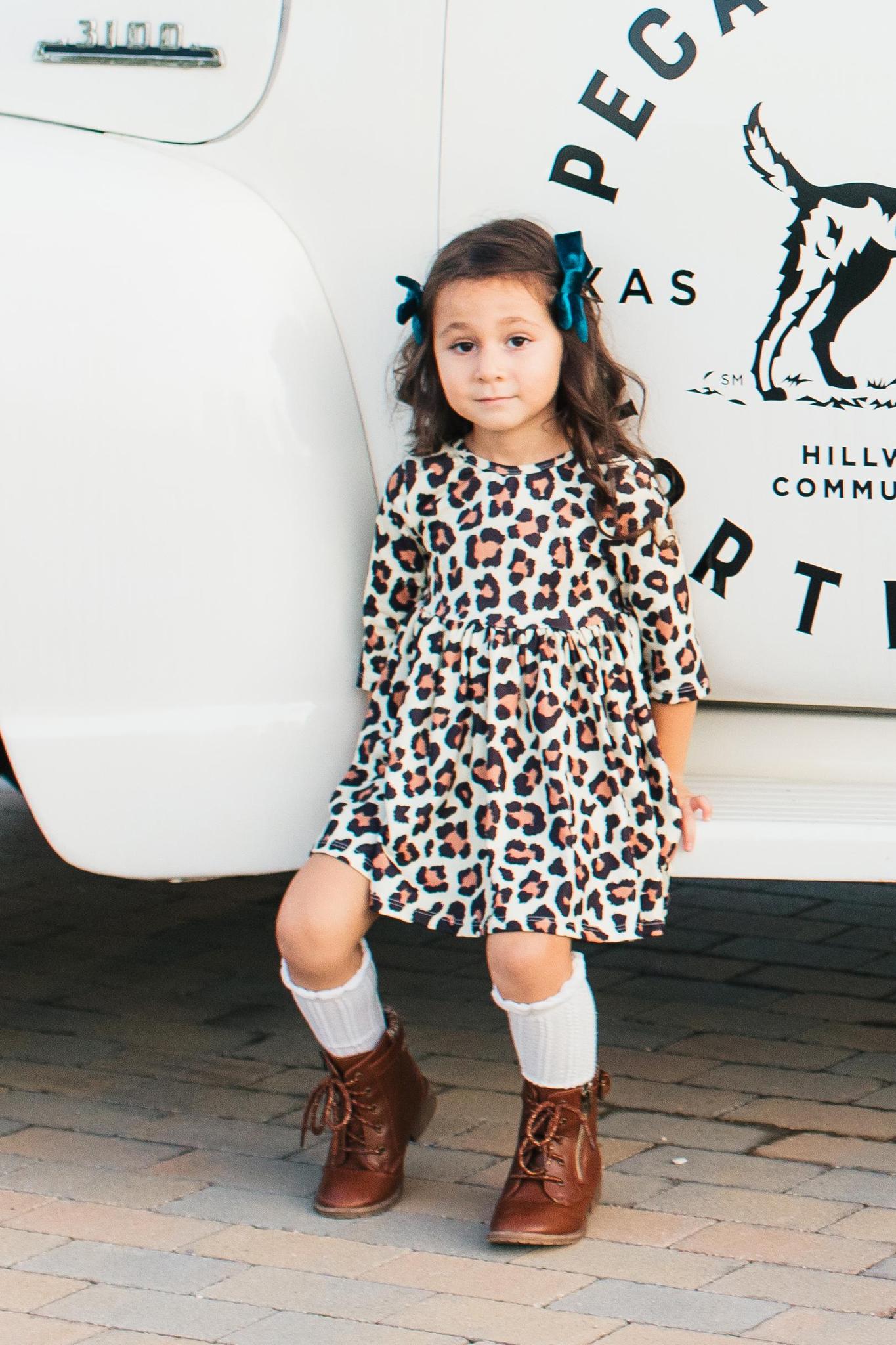 Young girl in a leopard print dress standing in front of a white vehicle with text and graphics.