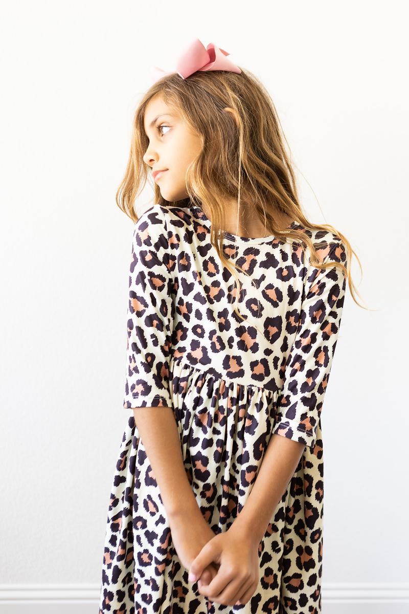 Girl wearing a leopard print dress with a pink headband against a white background