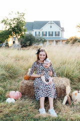 Woman and child sitting on a hay bale in a field with pumpkins and a house in the background