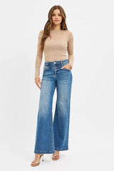 Woman wearing a beige long-sleeve top and blue jeans on a white background