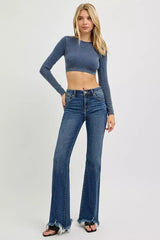 Woman wearing a blue cropped sweater and flared jeans on a white background