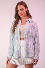 Woman wearing a colorful striped shirt over a white top and pleated skirt on a light pink background
