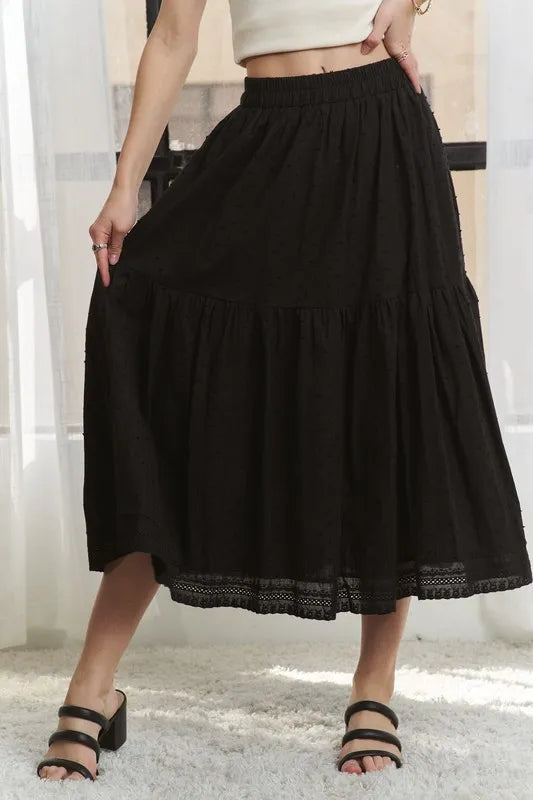 Person wearing a black tiered skirt with lace trim on a neutral background