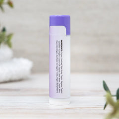 Lip balm with purple cap and white body on a light wooden surface.