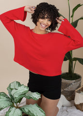 Woman wearing a red sweater and black shorts standing in a room with plants.