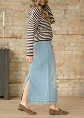 Woman wearing a striped sweater and denim skirt against a stone wall.
