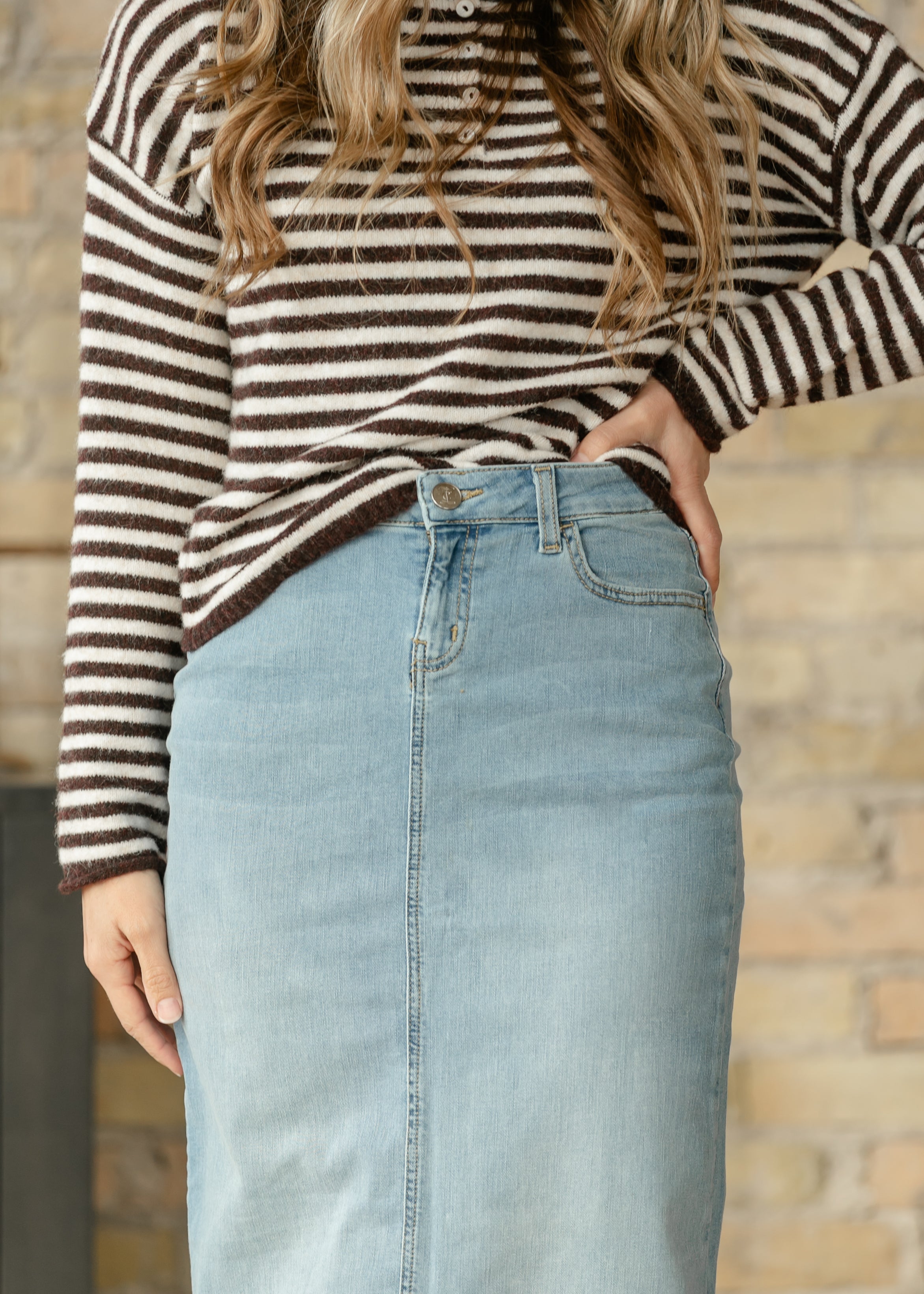 Person wearing a striped sweater and denim skirt against a wooden wall.