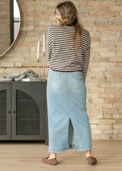 Woman wearing a striped sweater and denim skirt standing in a room with a brick wall.