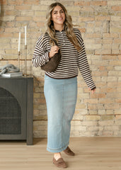 Woman wearing a striped sweater and light blue jeans standing against a stone wall.