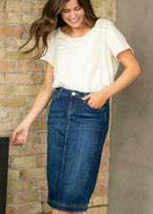 Woman wearing a white blouse and blue denim skirt against a brick wall.