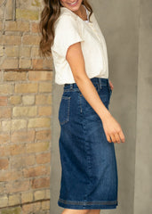 Woman wearing a white blouse and blue denim skirt against a stone wall.