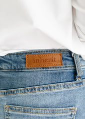 Close-up of blue jeans with 'inherit' brand label on a white background