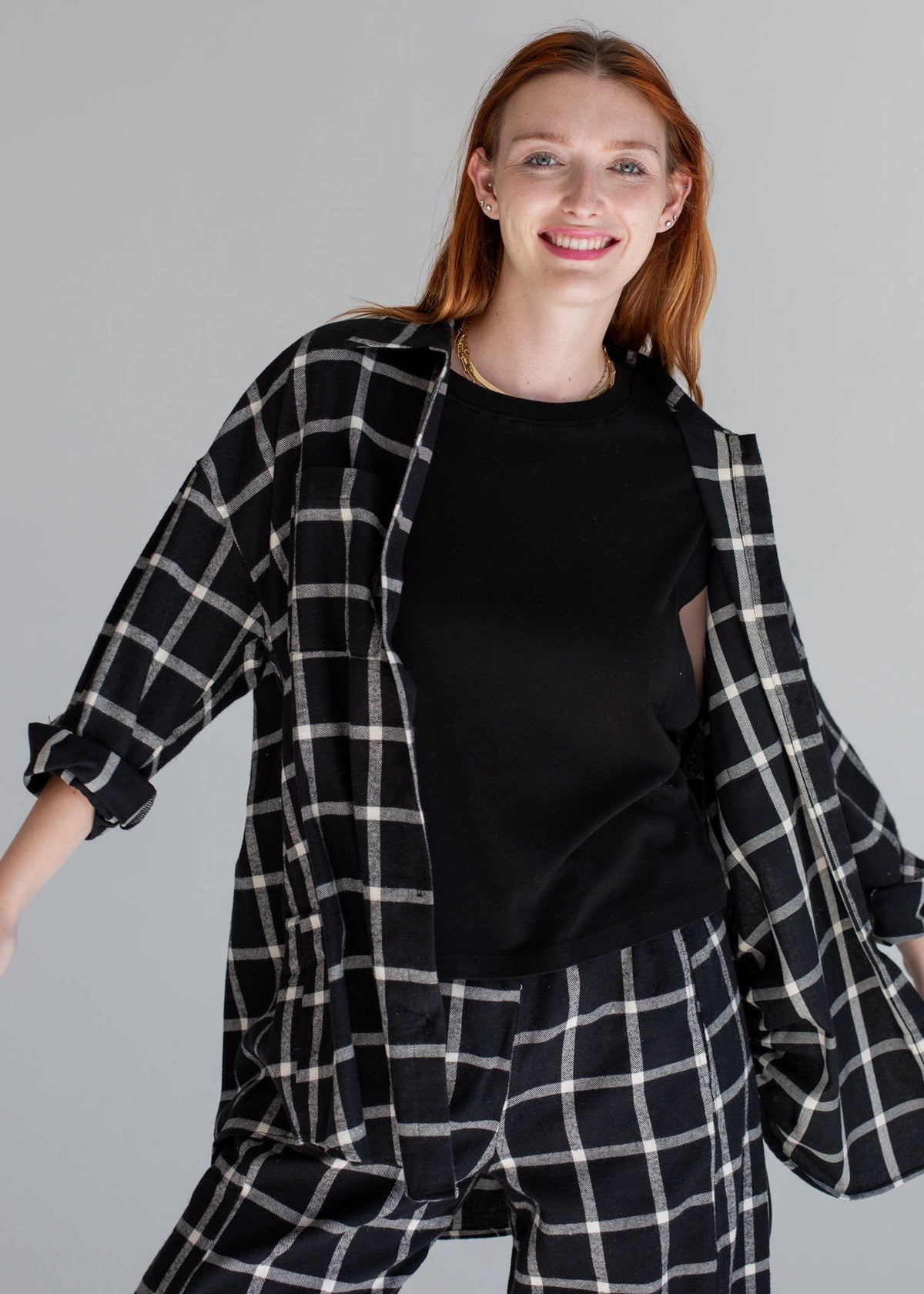 Woman wearing a black and white checkered shirt over a black top on a gray background