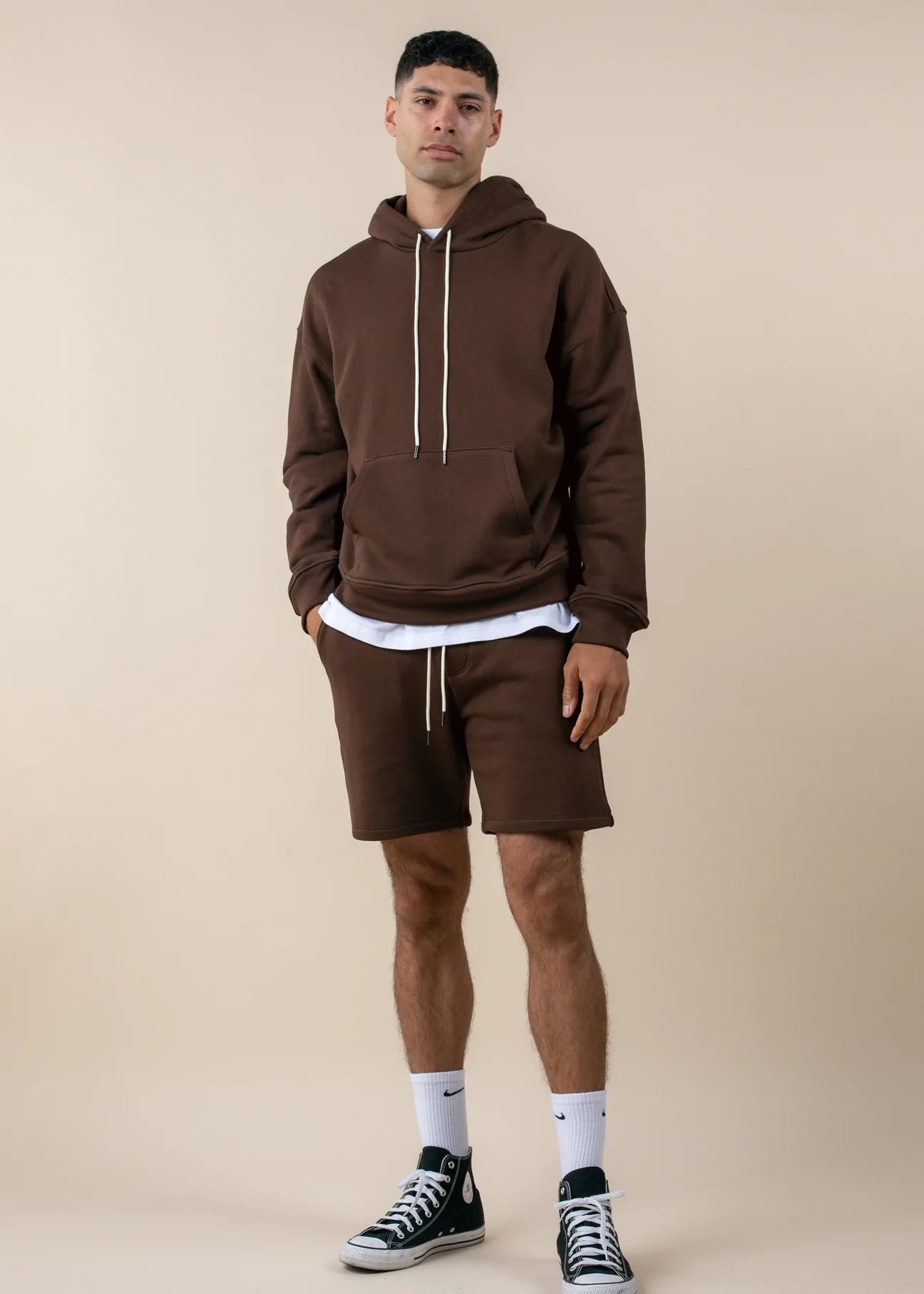 Man wearing a brown hoodie and shorts set on a beige background