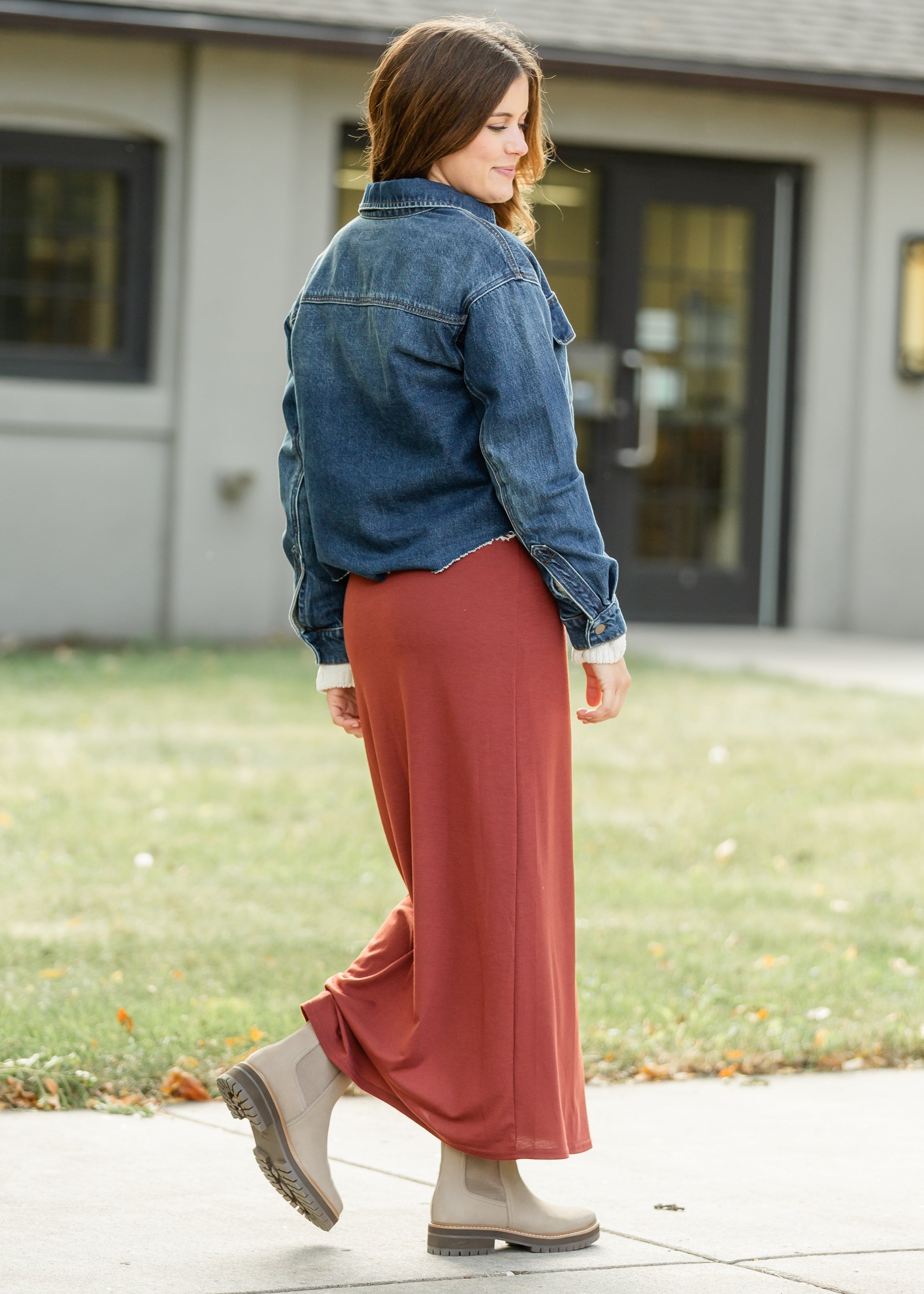Woman wearing a denim jacket and rust-colored pants walking outdoors.