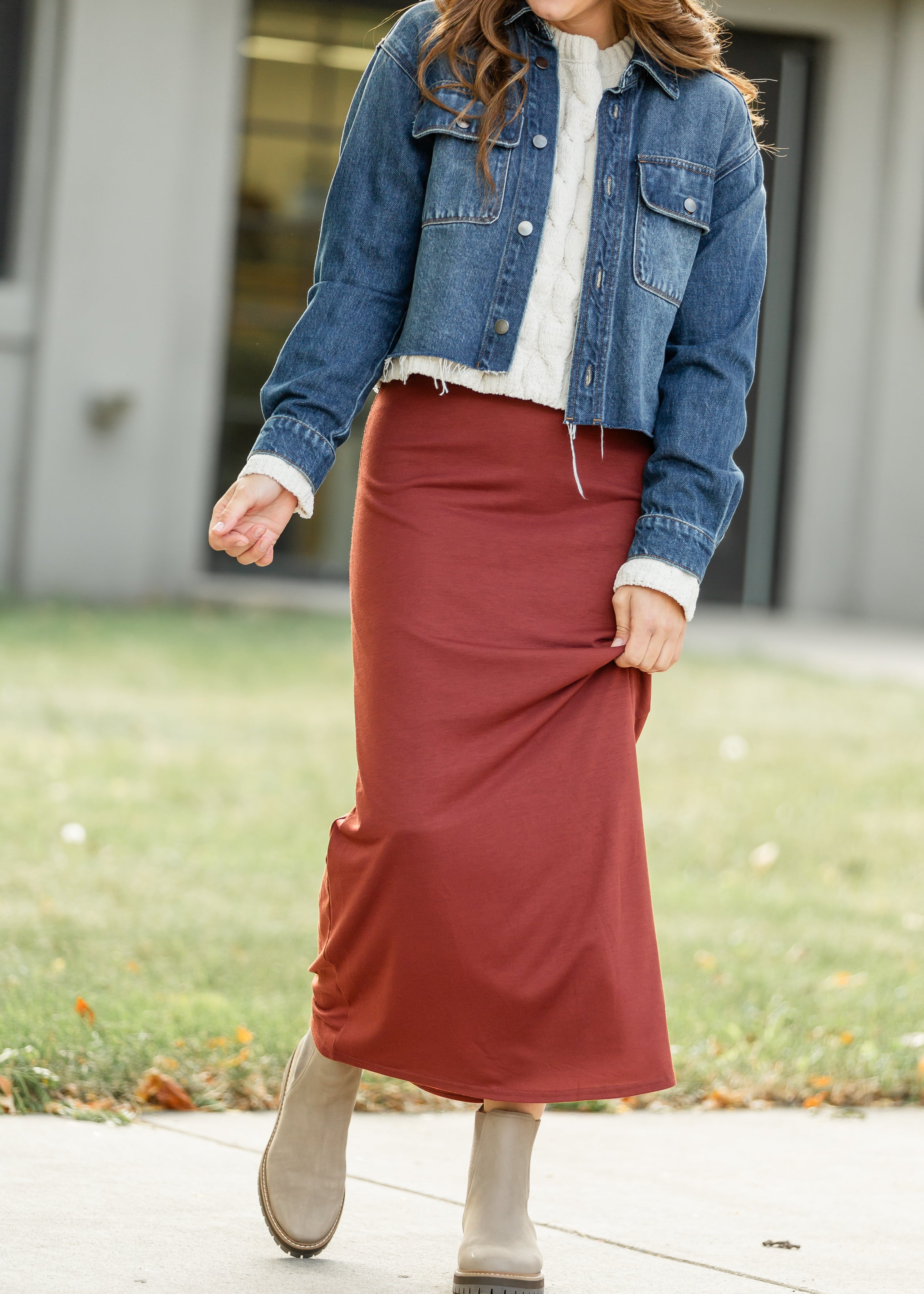 Person wearing a denim jacket, white shirt, and red skirt outdoors.