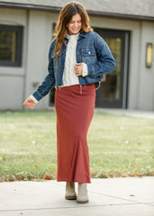 Woman wearing a denim jacket, white sweater, and red skirt outdoors.