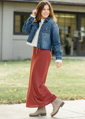 Woman wearing a denim jacket, white shirt, rust-colored pants, and brown boots outdoors.