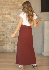Woman wearing a white top and red skirt standing against a brick wall.