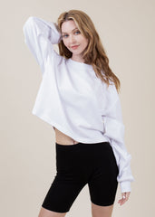 Woman wearing a white oversized sweatshirt and black shorts on a beige background