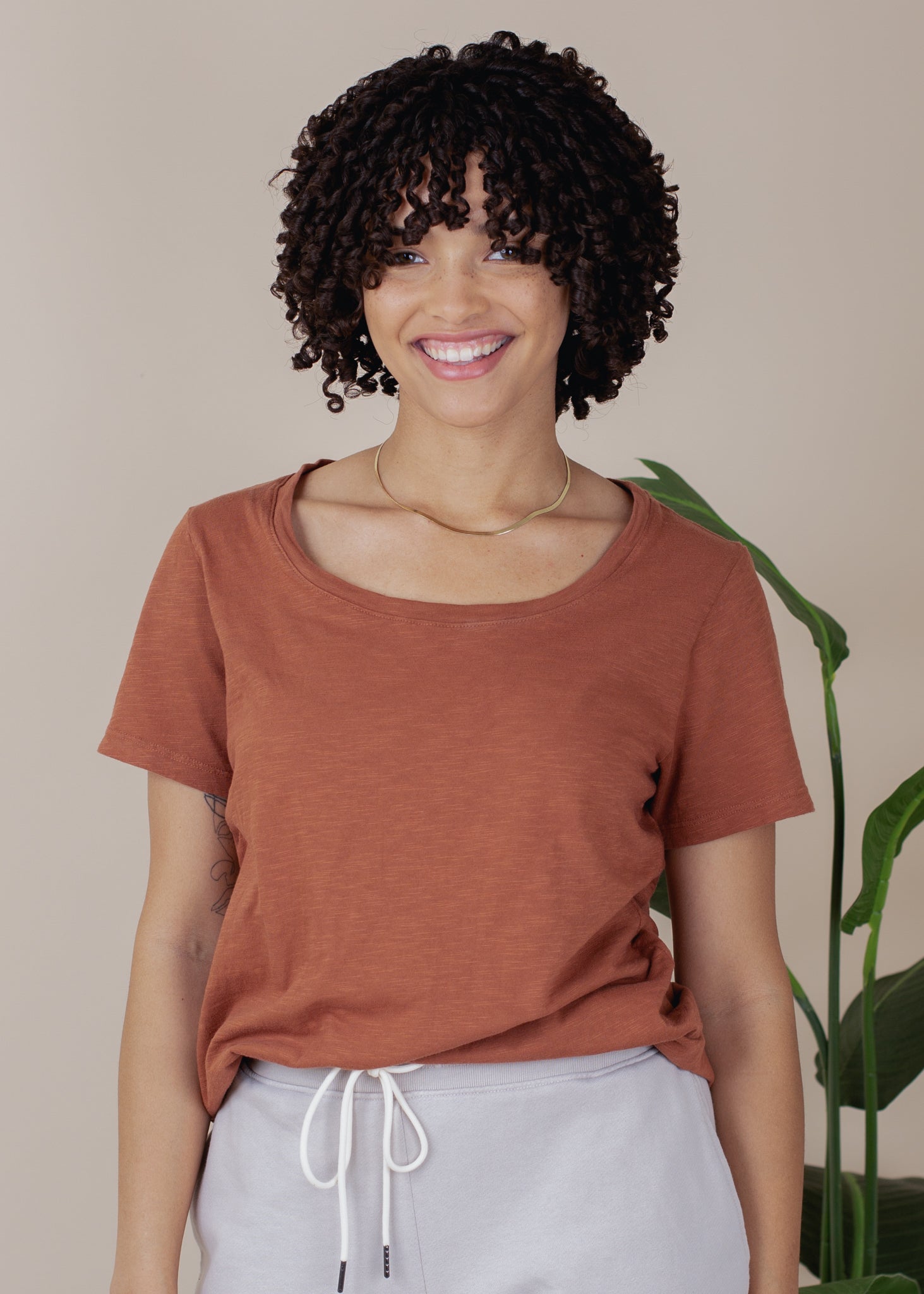 Person wearing a brown t-shirt and gray pants with a plant in the background