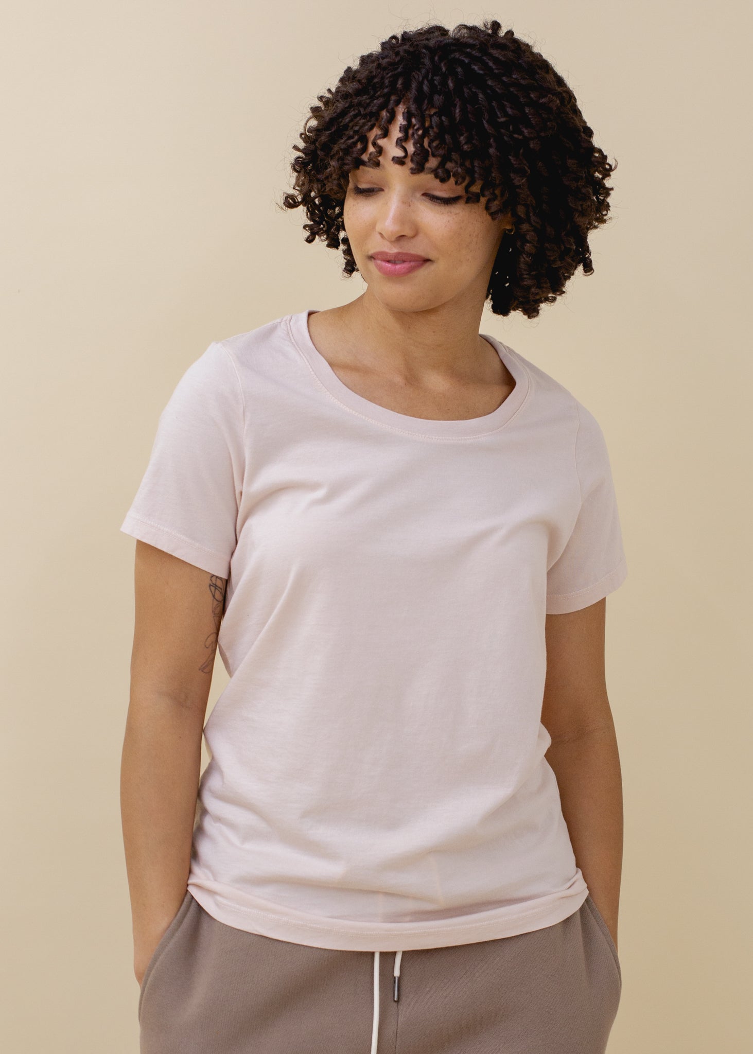 Woman wearing a light pink t-shirt against a beige background