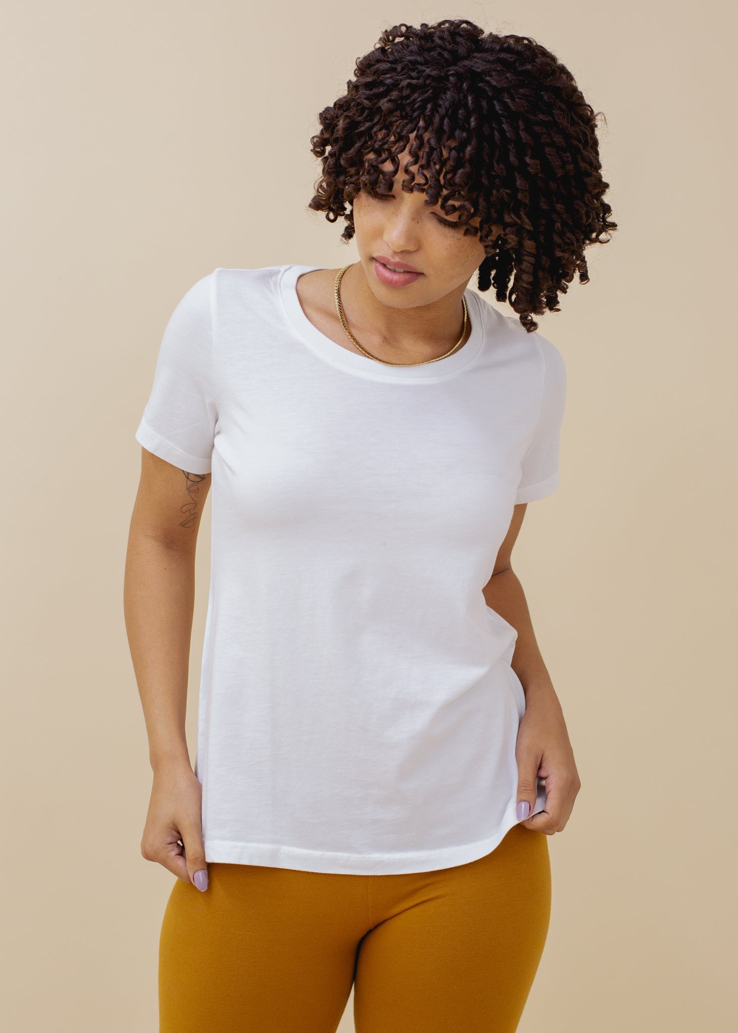 Woman wearing a white t-shirt and mustard pants against a beige background