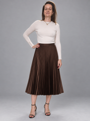 A woman modeling a brown pleated midi skirt with a white long-sleeve top and black high-heeled sandals, standing against a solid gray studio background.
