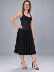 A woman modeling a black sleeveless midi dress with a structured corset-style bodice and a pleated skirt, paired with black heeled sandals, against a solid gray studio background.
