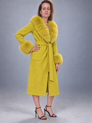 A woman models a bright yellow faux fur coat with a matching belt and large faux fur collar and cuffs, paired with black high-heeled sandals, against a gray studio background.