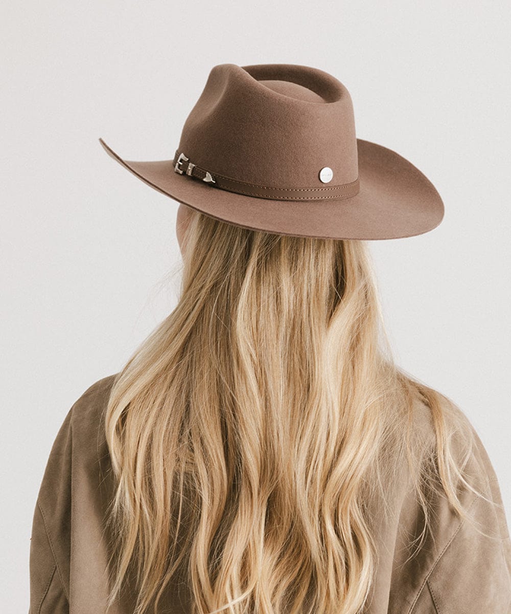 Person wearing a brown fedora hat with a plain background
