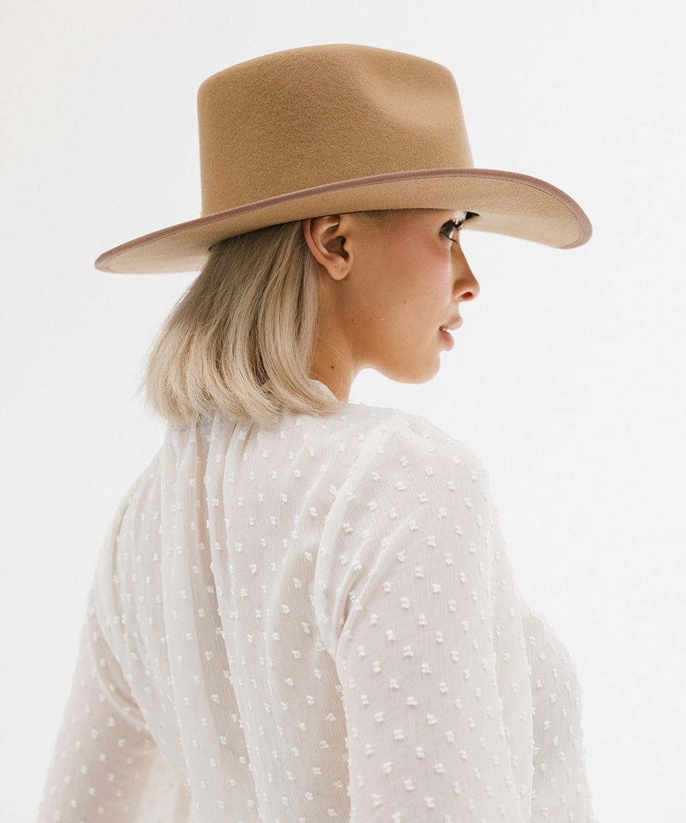 Woman wearing a beige hat and white polka dot shirt on a light gray background