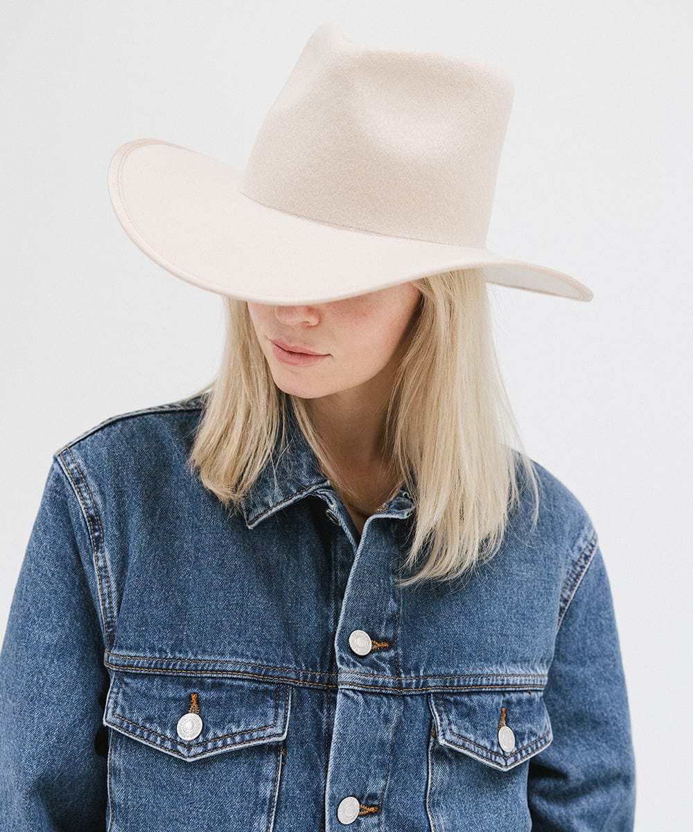 Person wearing a denim jacket and beige hat on a light gray background