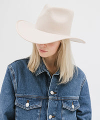 Person wearing a denim jacket and beige hat on a light gray background
